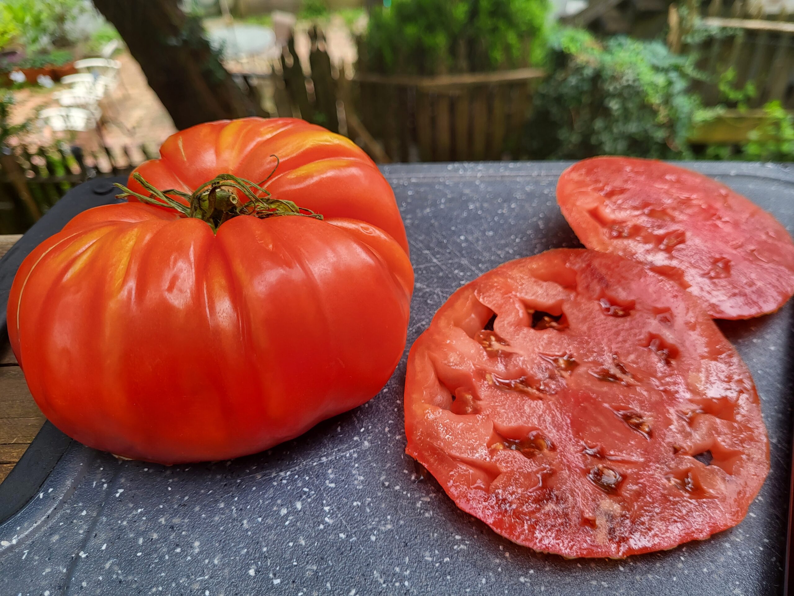 Heirloom tomato with slices on dark cutting board background juicy red and vibrant